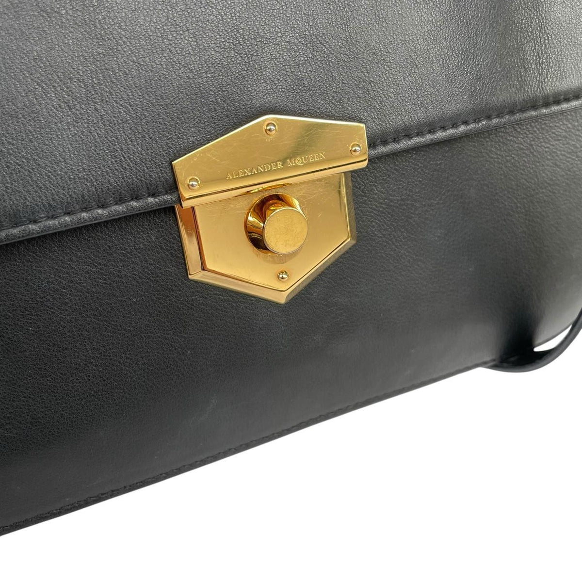Alexander McQueen black and gold leather messenger bag with logo detailing and faint scratches.