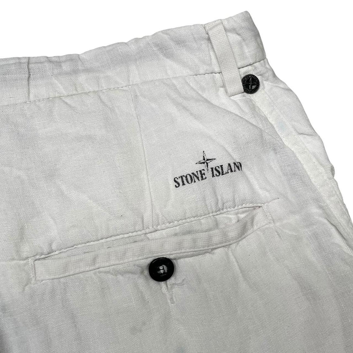 Stone Island white linen Bermuda shorts with logo patch and subtle stains.