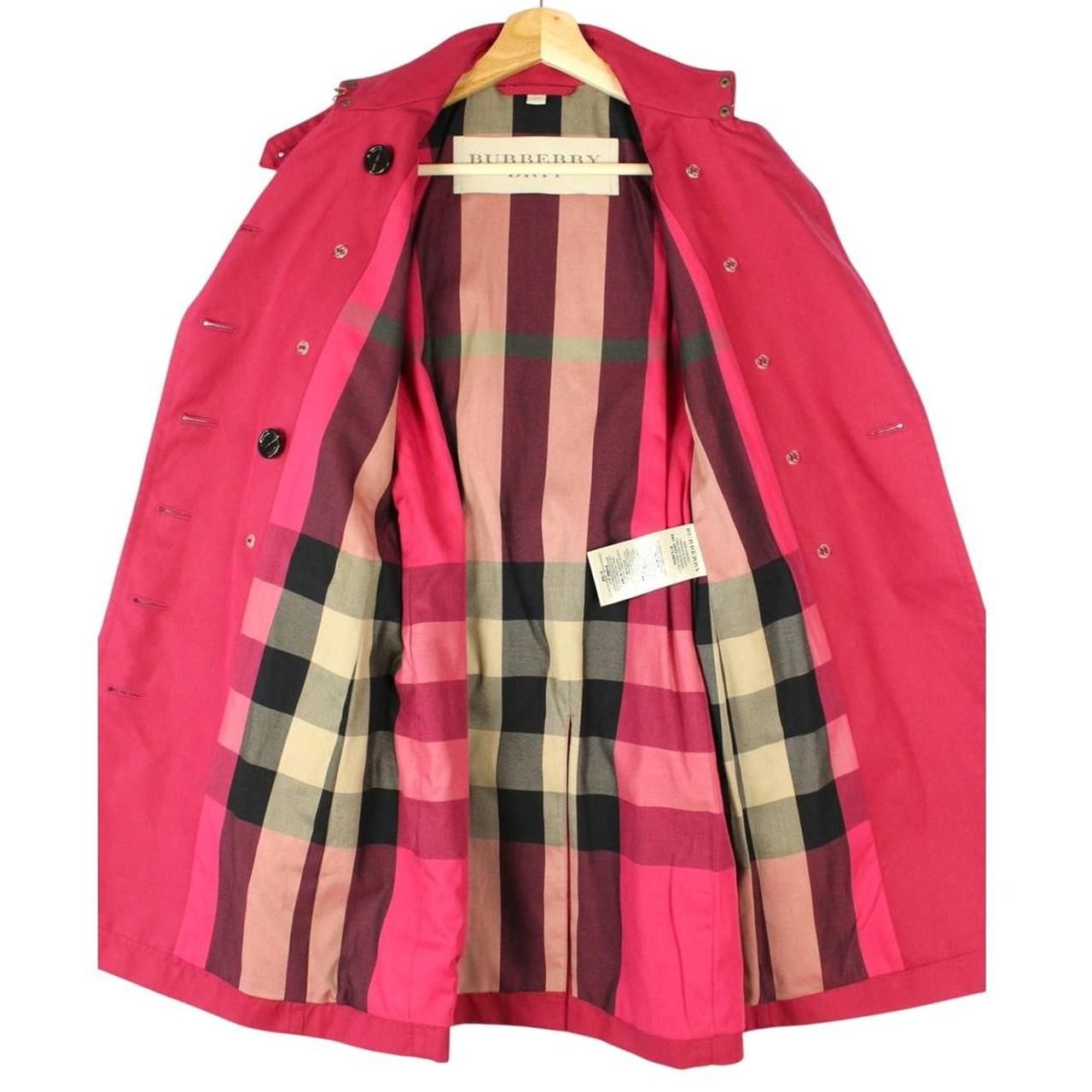 Burberry pink double breasted belted trench coat with classic check lining and logo buttons.