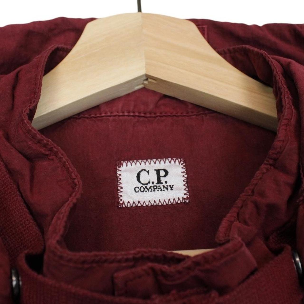 CP Company burgundy jacket with goggle detail and full zip closure.