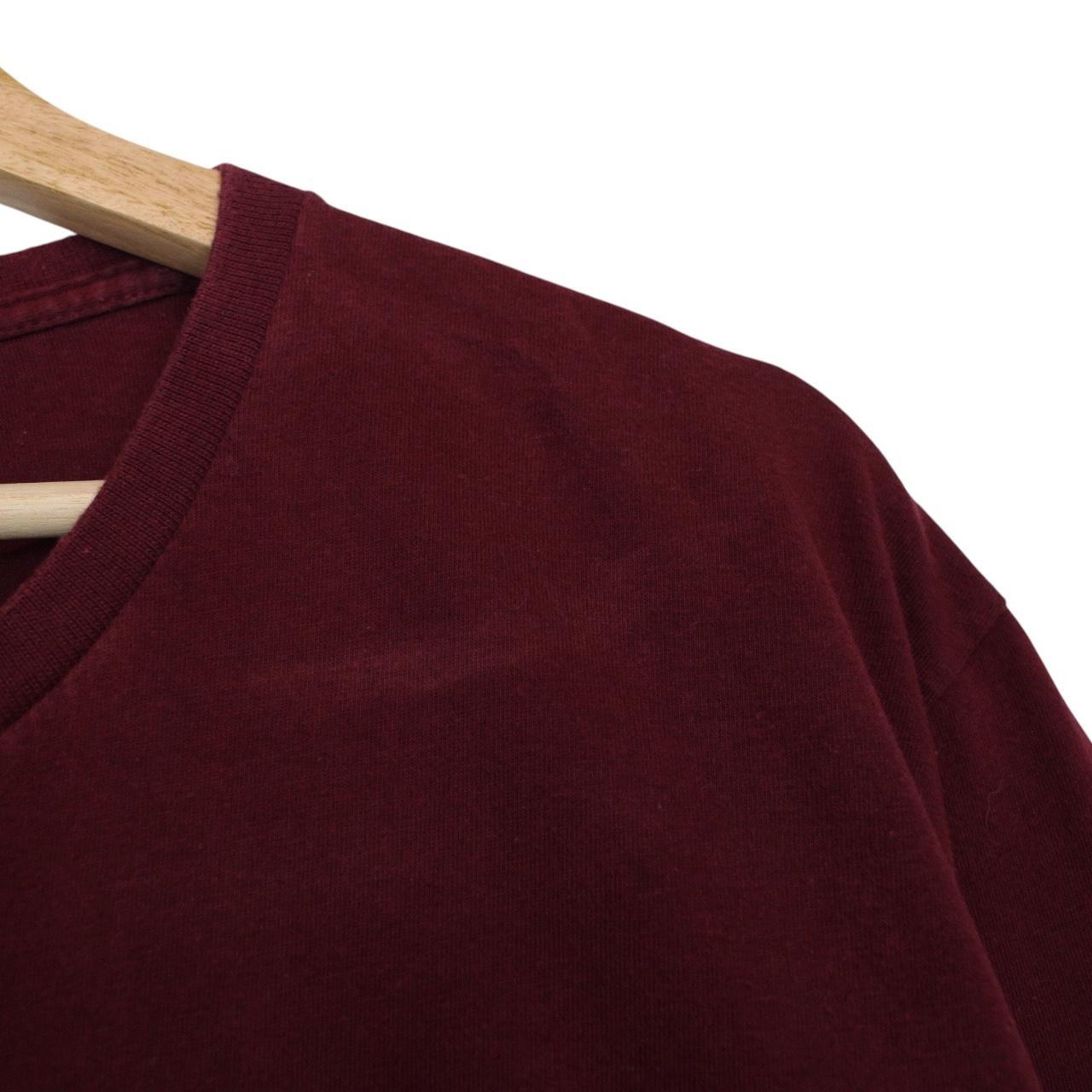 Stüssy burgundy pocket t-shirt with yellow college print and faint shoulder mark.